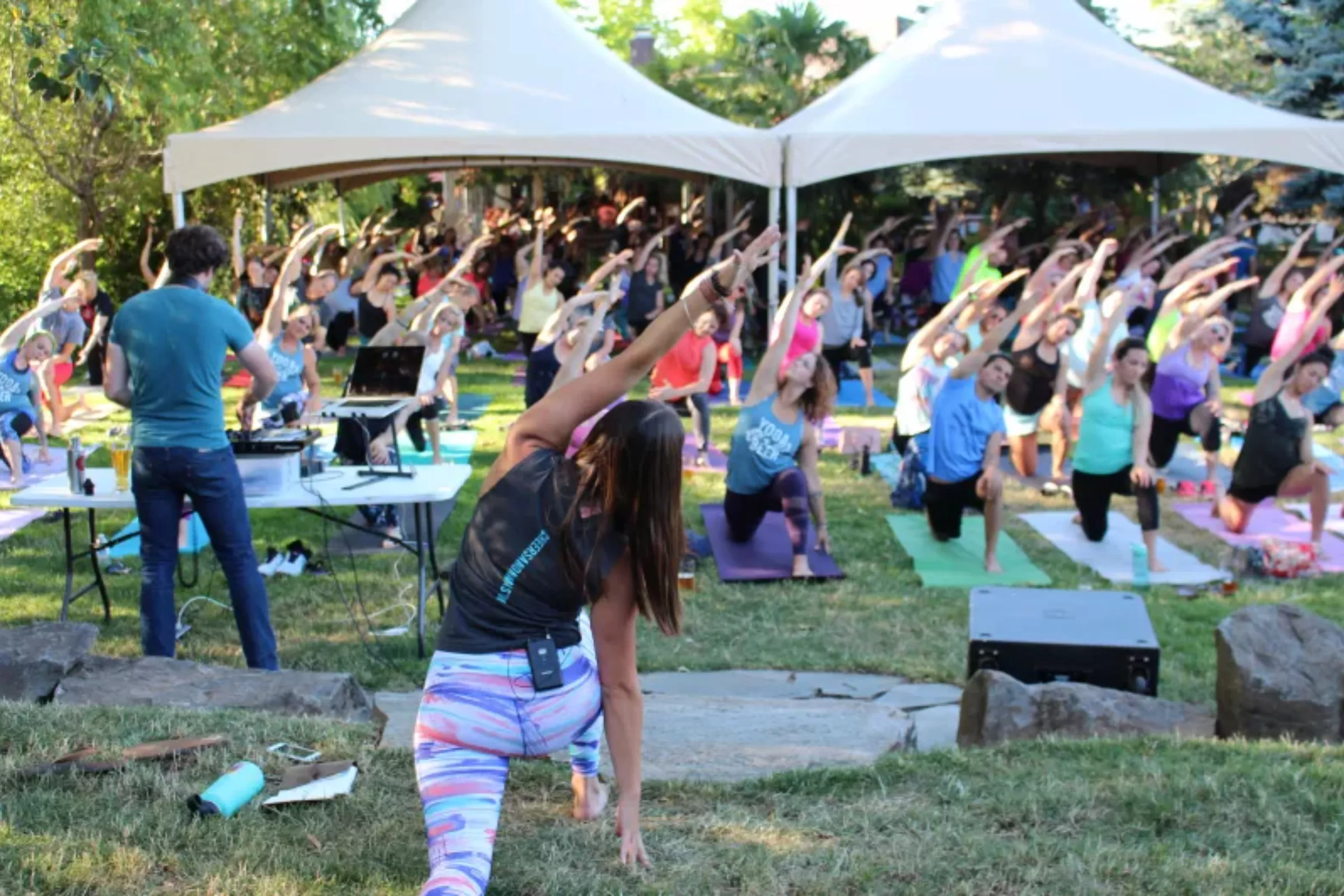 A group perform yoga outside with an instructor and dj in the foreground